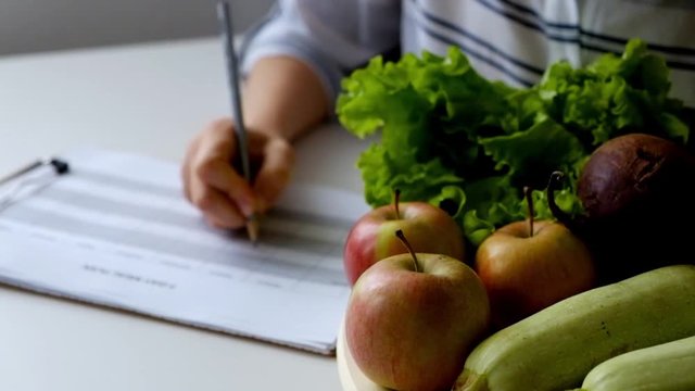 Woman writing diet plan on table full of fruits and vegetables