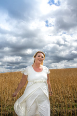 Ausgelassene Frau in weißem Kleid auf Feld vor bewölktem Himmel