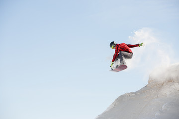Naklejka na ściany i meble Image of man in helmet with snowboard jumping from snowy mountain slope