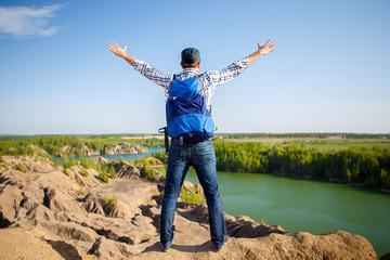 Image from back of young tourist with backpack with hands up against background of mountain landscape, lake