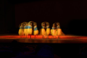 A group of people dancing on stage against black background. 