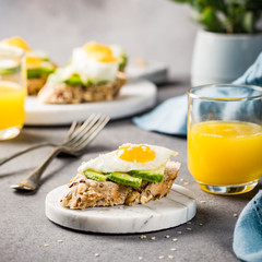 Healthy sandwich with fresh avocado and fried quail egg on small marble board on gray background. Breakfast or lunch food concept.
