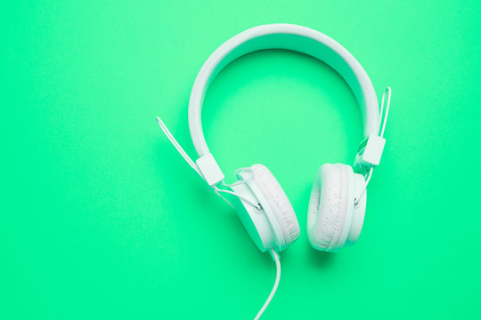 White headphones with cord on an empty green background.