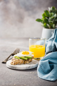 Healthy sandwich with fresh avocado and fried quail egg on small marble board on gray background. Breakfast or lunch food concept with copy space.