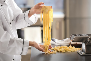 Female chef holding uncooked pasta near table - Powered by Adobe