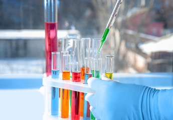Lab worker taking sample from test tube with green liquid, closeup