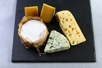 Cheese market - camembert, salty blue cheese and gauda. Cheese plate. Assortment of cheese on a stone plate. close up. set