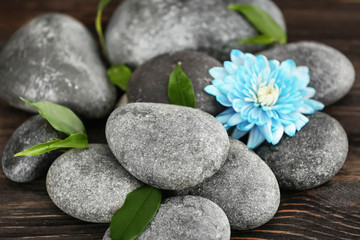 Spa stones with beautiful flower and green leaves on wooden table