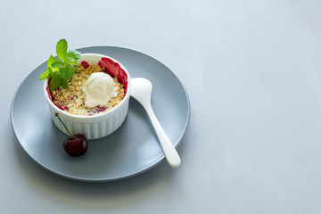 Cherry crumble with oatmeal and ice cream in bowl on grey wooden desk. Summer healthy food