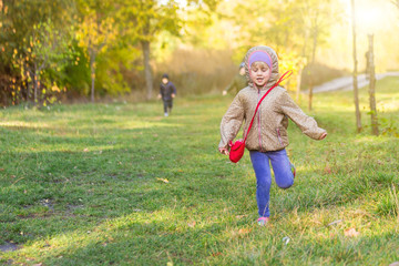 Little blond caucasian girl running in park or forest on bright autumn day. Child having fun playing outdoors. Happy healthy childhood activity and leisure concept