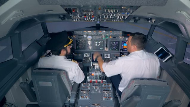 Two pilots are sitting in an airplane cabin and discussing something