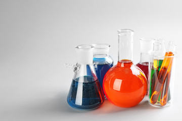 Chemical glassware with colorful liquids on light background