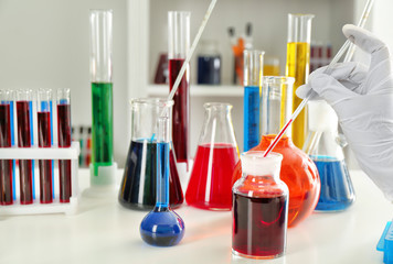 Lab worker taking sample from flask with red liquid on table