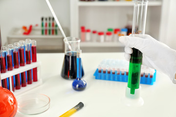 Lab worker holding test tube with green liquid near table