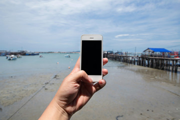 Hand hold white mobile phone with beautiful fresh sea and port.