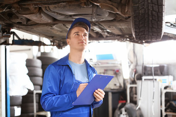 Male mechanic with clipboard examining car in service center