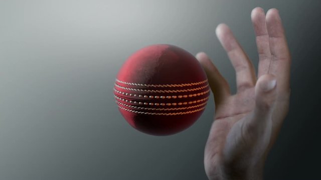 A closeup of a red cricket ball caught in ultra motion flying through the air about to be caught by a dirty hand