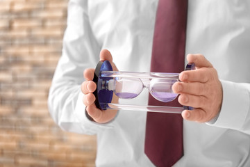 Man holding hourglass on blurred background, closeup. Time management concept