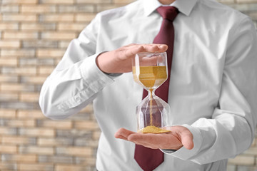 Man holding hourglass on blurred background, closeup. Time management concept