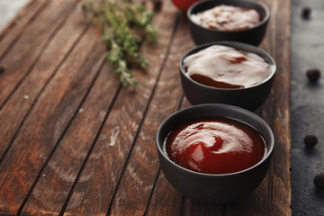 Delicious barbecue sauces in bowls on wooden board