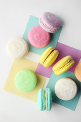 Tasty colorful macarons with sheets of paper on white background