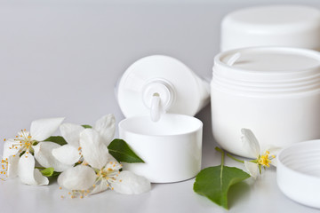 Fototapeta na wymiar Cosmetics in white jars and a soft cream in a tube on a light background and spring flowers. Free space for text. Still life