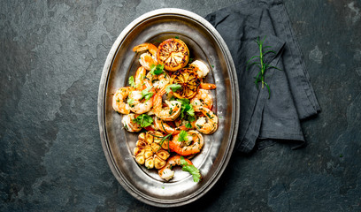 Grilled roasted shrimps prawns on oval metal vintage plate, top vie. Slate background