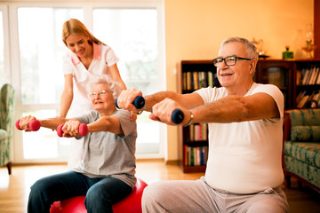 Nurse at nursing home helps senior people to doing exercises