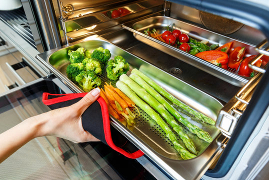 Woman's hand taking out steamed  vegetables out of a steam oven