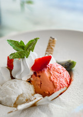 three flavored ice cream scoops on plate, with strawberry and mint on table