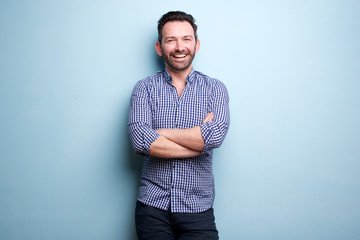 cheerful man with beard posing against blue wall with arms crossed