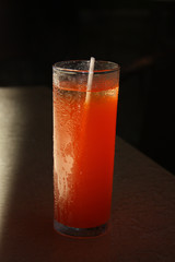 Orange tropical drink in clear glass with condensation on outside and white straw inside