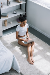 high angle view of african american girl using laptop white sitting on floor in bedroom