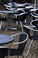 Fototapeta na wymiar Vacant tables and chairs with shiny metal backrests at street cafe. Selective focus on foreground chair