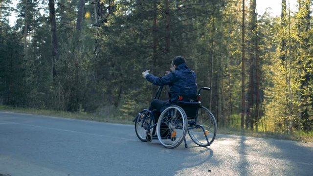 Training wheelchair is getting moved along the road by a disabled man