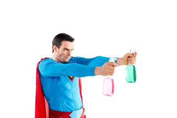 confident superhero holding plastic spray bottles with cleaning liquid and looking away isolated on...