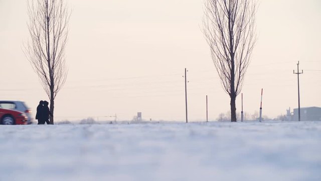Cold white winter landscape with people and vehicles passing 4K. Long shot panning of two people in focus walking from left to right with many cars passing over the frame.