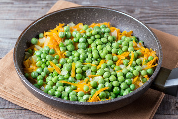 Peas, onions and carrots on a frying pan