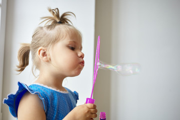 Profile picture of adorable little girl of Caucasian appearance pouting her lips while blowing soap bubbles against white wall background with copy space for your text or advertising information © Anatoliy Karlyuk