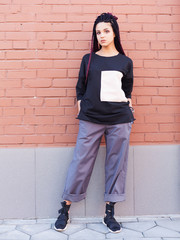 Fashion streets. Young beautiful girl in fashionable cool young clothes from designer posing near brick wall in city