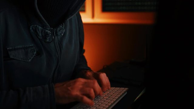 Computer hacker typing keyboard in dark interior