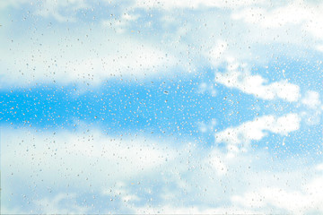 drops of rain on glass on background of blue sky with clouds