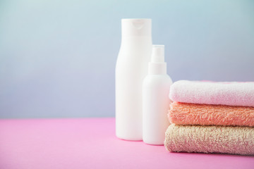 Fototapeta na wymiar bath accessories - towels folded and shampoo , stacked on a light, bright blue and pink background The concept of caring for yourself, your body. Copy space