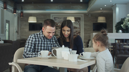 Daughter trying to attract parent's attention while they are busy looking in tablet. She looked bored.