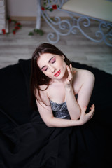 Naklejka premium Beautiful girl in black long dress in white interior, model woman sits on the floor with white parquet.