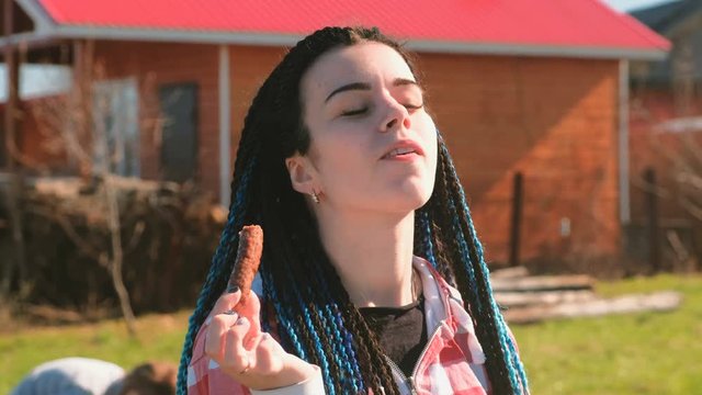 Woman eating meat sausage in the backyard in the spring on a Sunny day. Her son plays around.