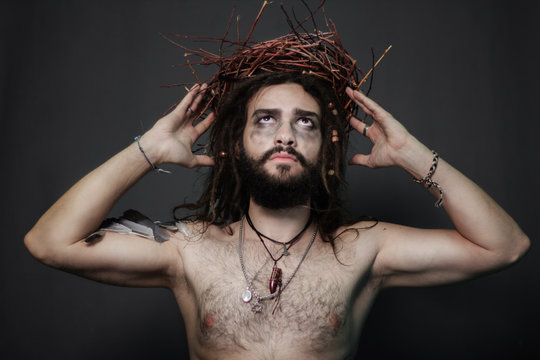 The image for halloween. A brutal guy with dreadlocks on a gray background. The guy with a thick beard. Hand the bird's wing. Feathers on hand. Fantasy. Crown of wreaths on head