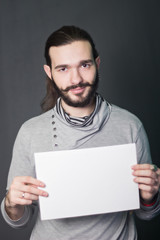 A bearded guy. Hipster model. fashion portrait in studio on a gray background with a piece of white paper in hands