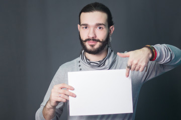 A bearded guy. Hipster model. fashion portrait in studio on a gray background with a piece of white paper in hands