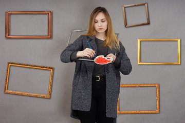 Young artist with palette and picture frames in grey coat on grey background